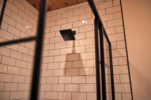 Un área de ducha con paredes de azulejos blancos y un cabezal de ducha negro.