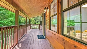 A wooden deck with a wooden railing, large windows, and a door with a doormat.