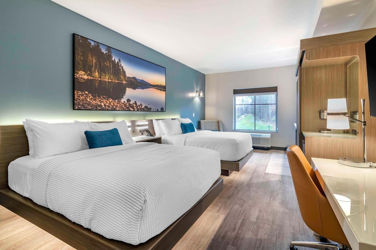 A hotel room with two beds, a desk, a chair, a large window, and a painting on the wall.