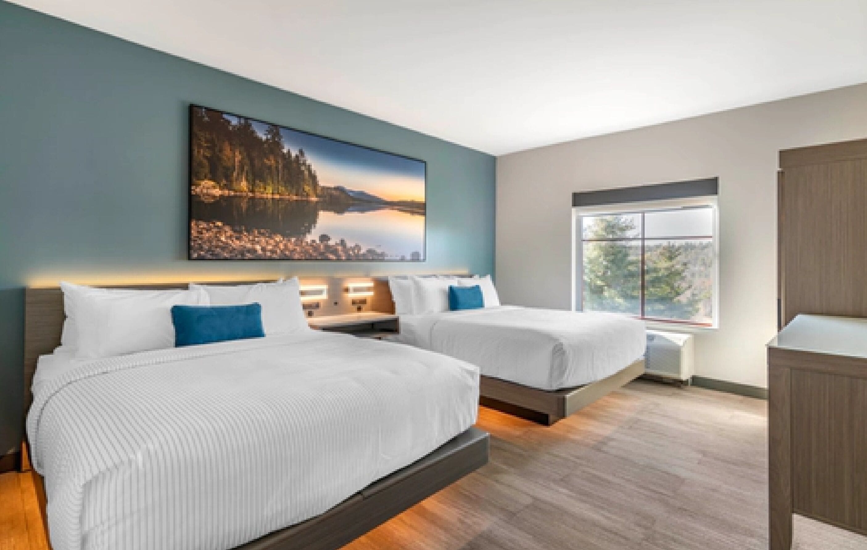 A modern hotel room with two beds, a large window, and a cityscape painting on the wall.