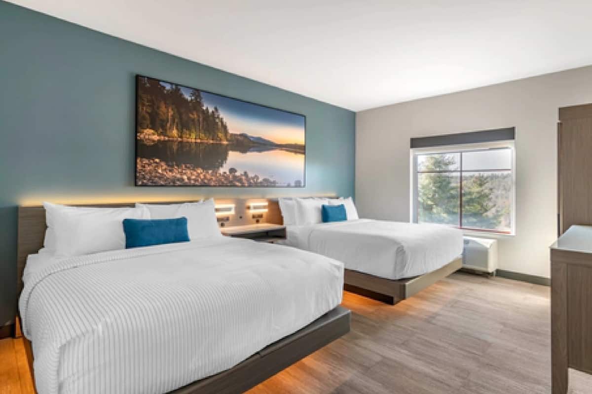 A modern hotel room with two beds, a large window, and a cityscape painting on the wall.