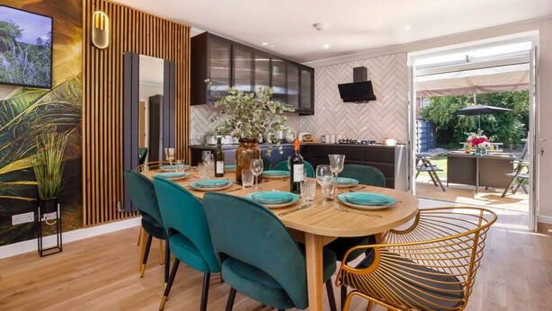 Un espace repas moderne avec des chaises de couleur turquoise, une table en bois et une cuisine en arrière-plan.