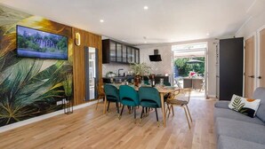 Un salon moderne avec un canapé gris, un coin repas avec des chaises turquoise et une cuisine avec des meubles noirs.