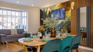 Un coin repas avec une table ronde en bois, dressée pour six personnes, entourée de chaises de couleur turquoise.