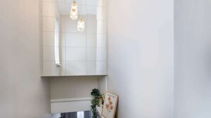 Une salle de bain avec un mur recouvert de carreaux blancs, une serviette blanche suspendue à un porte-serviettes et un tableau encadré posé sur le sol.
