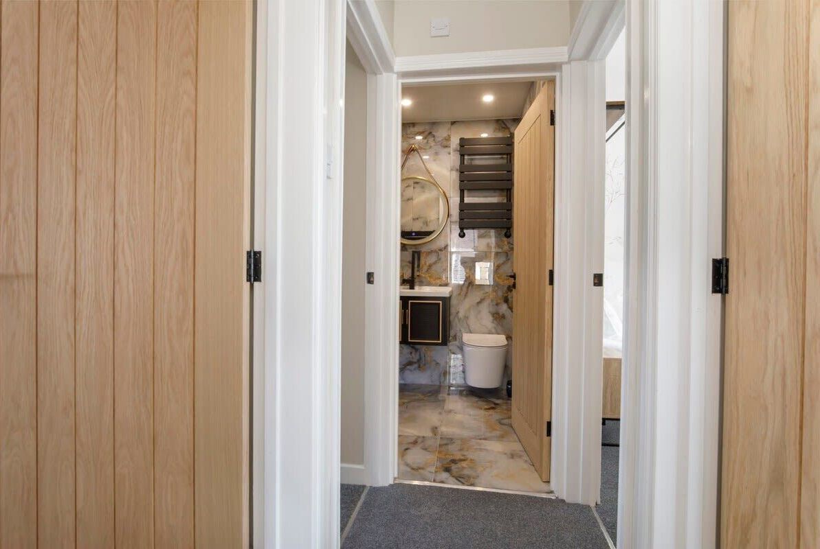 A hallway with wooden doors and a marble floor leading to a bathroom with a sink and mirror.
