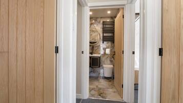 A hallway with wooden doors and a marble floor leading to a bathroom with a sink and mirror.