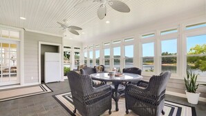 Eine überdachte Terrasse mit Korbmöbeln, großen Fenstern und einem Deckenventilator.