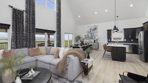 A spacious living area with a grey sectional sofa, a coffee table, and a dining area with a small island. The kitchen is modern with dark cabinets and a large island.