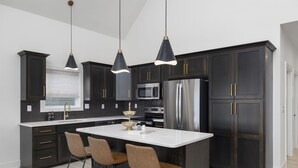 A modern kitchen with dark cabinetry, a white island, stainless steel appliances, and pendant lighting.