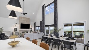 A modern living room with a fireplace, a dining area with a table set for four, and a balcony with a view.
