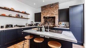 Une cuisine moderne dotée d’un îlot central, de meubles de rangement aux couleurs sombres et d’une cheminée en briques.