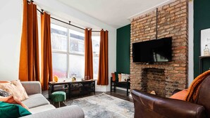 Un salon avec une cheminée en briques, un téléviseur à écran plat fixé au-dessus, un canapé, une table basse et une fenêtre avec des rideaux.