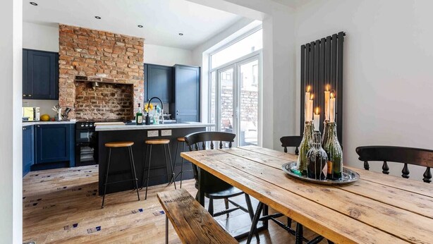 Une cuisine moderne avec un mur en briques, des meubles de couleur sombre et une table à manger en bois décorée de bougies.