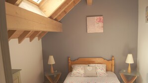 A bedroom with a sloped ceiling, a bed with patterned bedding, two bedside tables with lamps, and a framed picture on the wall. - Gîte Indépendant Dans Maison Propriétaires (Saint-Laurent-en-Grandvaux)