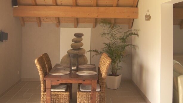 A dining area with a wooden ceiling, a chandelier, a dining table set with plates, and wicker chairs. - Gîte Indépendant Dans Maison Propriétaires (Saint-Laurent-en-Grandvaux)