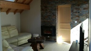 A cozy living room with a stone fireplace, a sofa, and a television. - Gîte Indépendant Dans Maison Propriétaires (Saint-Laurent-en-Grandvaux)