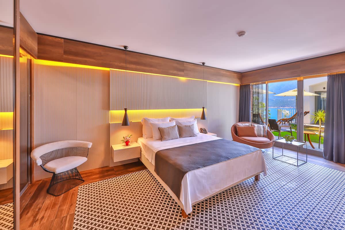 Una habitación de hotel moderna con una cama grande, una zona de estar y un balcón con vistas.