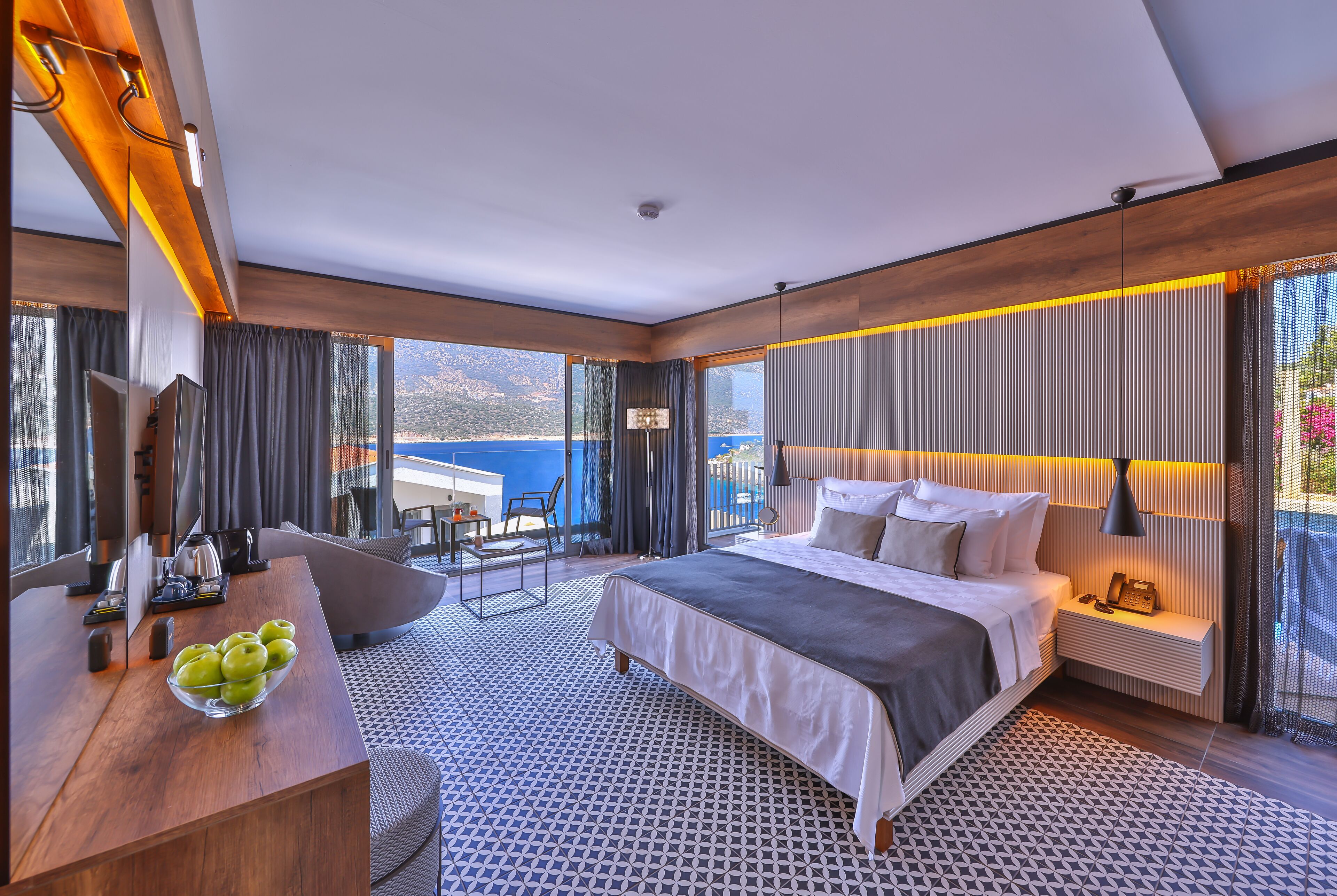 Een moderne hotelkamer met een groot bed, een bureau met een fruitschaal, een stoel en uitzicht op zee.