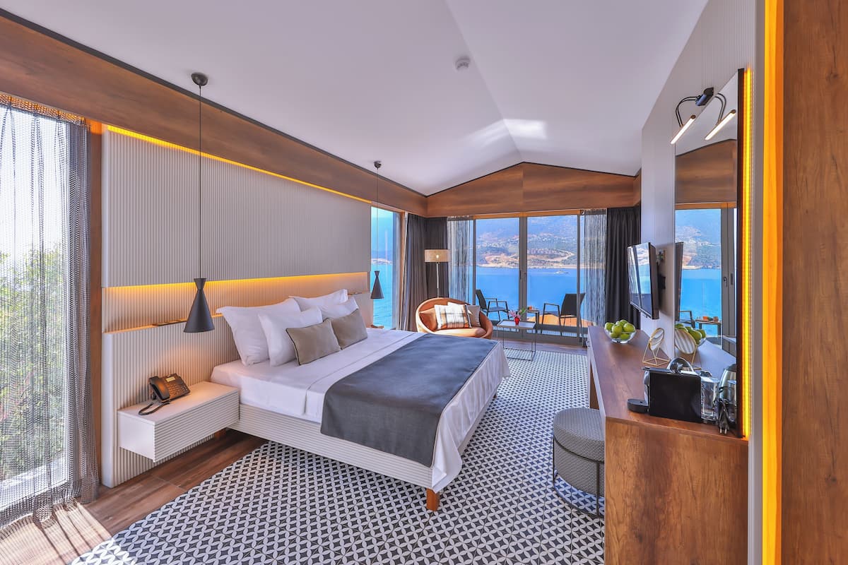 Una habitación de hotel moderna con una cama grande, un área de descanso con vistas y un balcón sobre el mar.