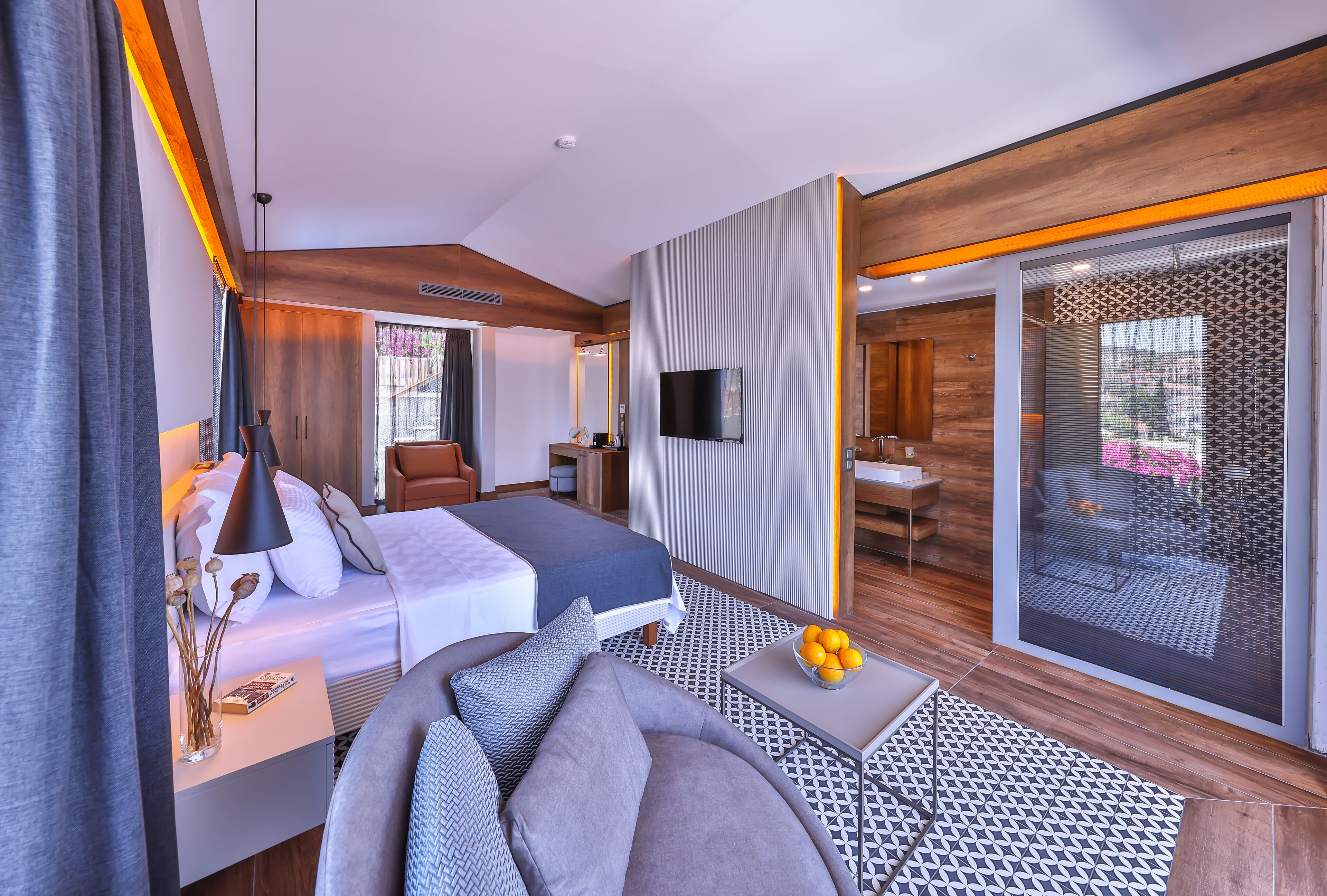 A modern hotel room with a bed, a sofa, a TV, and a balcony with a view.