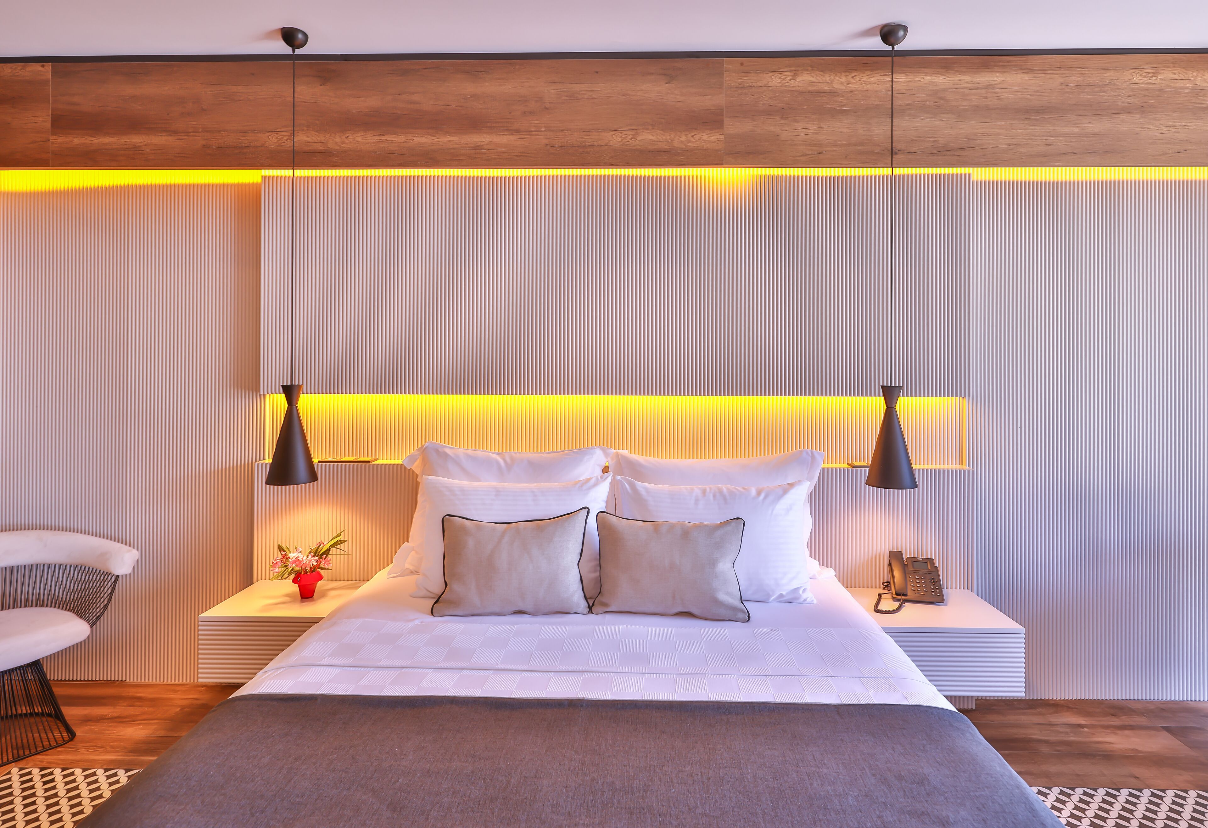 A modern bedroom with a large bed, bedside lamps, and a nightstand with a phone.