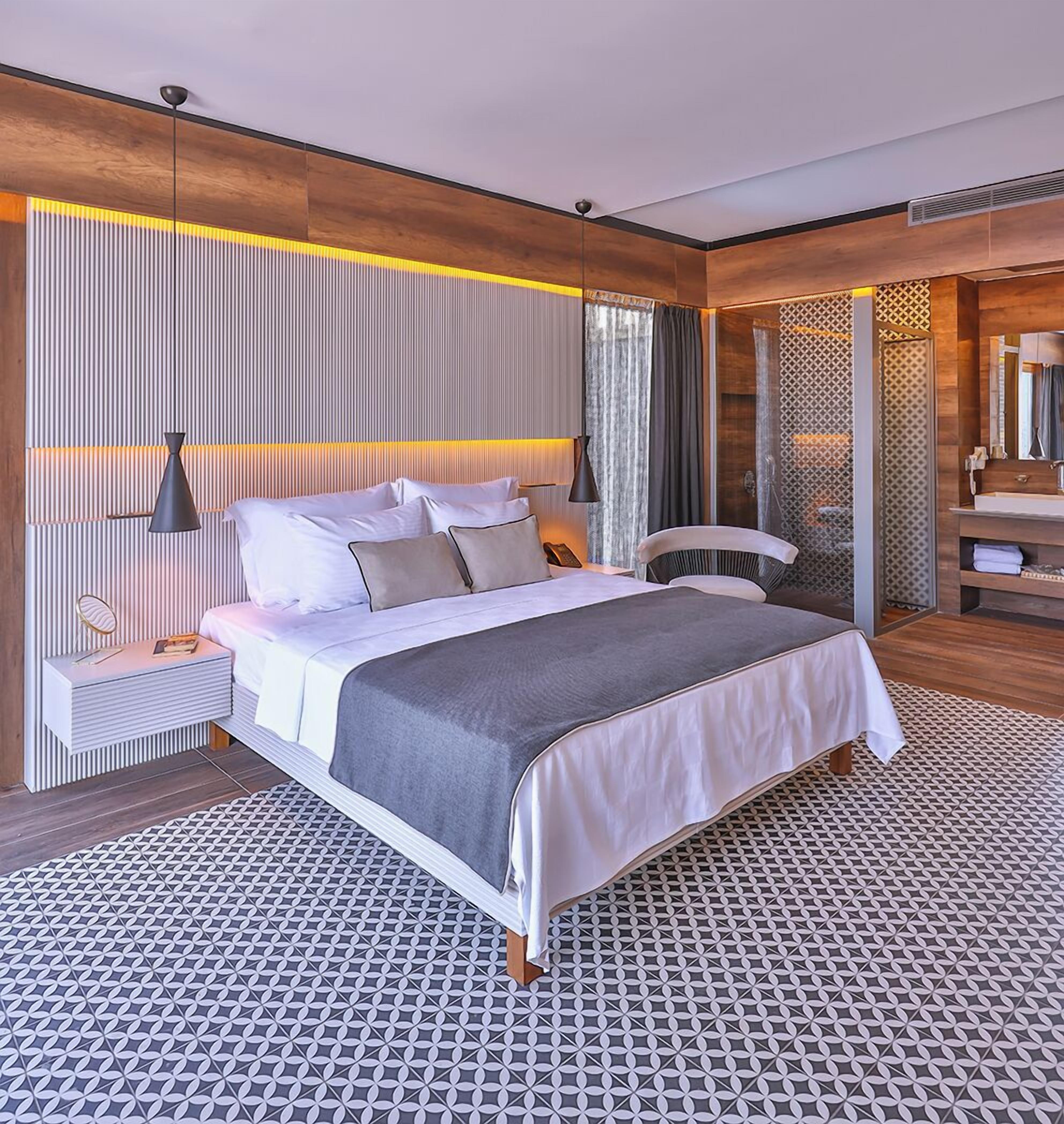 A modern bedroom with a large bed, bedside tables, a mirror, and a bathroom with a sink and mirror.