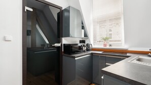 Una cocina moderna con armarios oscuros, microondas, cafetera y ventana con persianas.