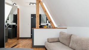Un dormitorio estilo loft moderno con techo inclinado, una viga de madera, un sofá y una cocina al fondo.