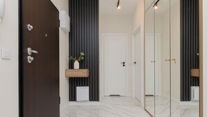 Un baño moderno con una puerta de madera oscura, un inodoro blanco, una planta pequeña en un estante y un espejo con marco negro.