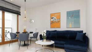 Una sala moderna con un sofá azul oscuro, una mesa redonda y un comedor con una mesa pequeña y sillas.