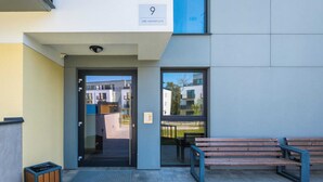 A building entrance with a glass door, a wooden bench, and a trash bin. - Modern Apartment with Terrace | Close to the Beach | Parking. (Jastrzebia Góra)