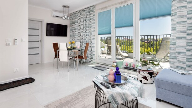 A modern living room with a dining area, large windows with blue blinds, and a balcony with outdoor furniture. - Modern Apartment with Terrace | Close to the Beach | Parking. (Jastrzebia Góra)