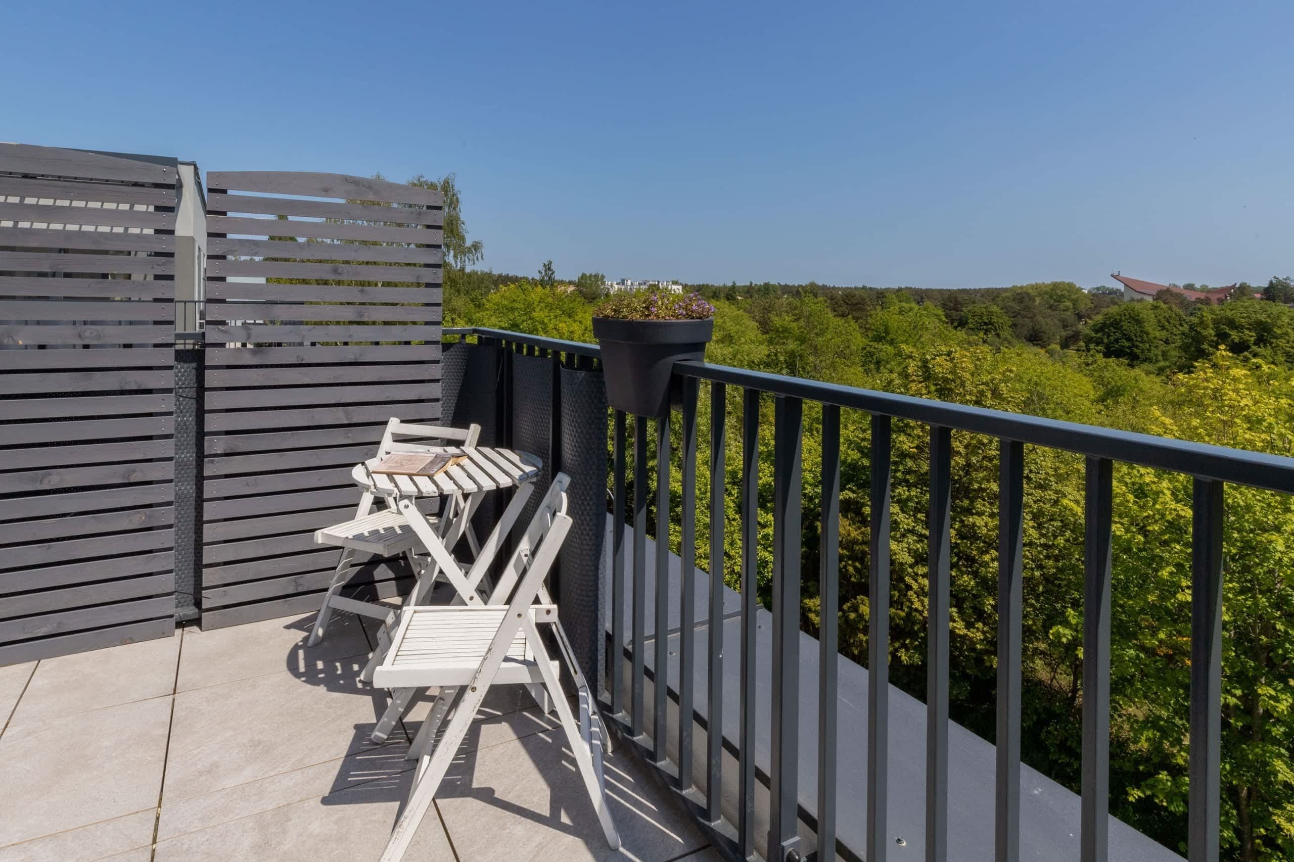 Een balkon met een metalen hekwerk, een witte klapstoel en een bloempot.
