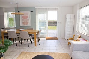 Un comedor con mesa y sillas de madera, un ventanal con persianas y vista a un jardín.