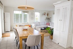 A dining area with a wooden table and chairs, a sofa, and a large white wardrobe.