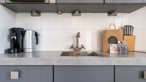 A modern kitchen with a stainless steel sink, a coffee maker, and a kettle on the countertop.