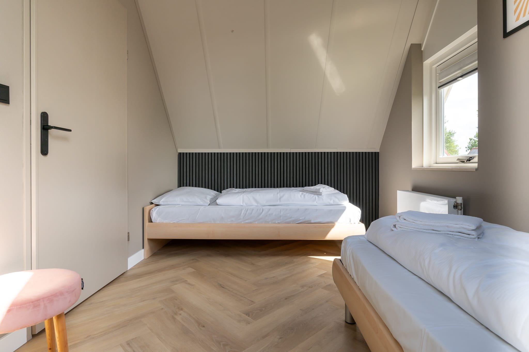 A bedroom with a loft bed, a bedside table, a chair, and a window.