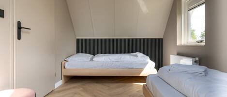 Een slaapkamer met een hoogslaper, nachtkastje, stoel en raam.