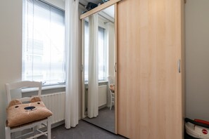 Una habitación con un radiador blanco, una silla con un cojín de oso de peluche, un armario de madera y una ventana con persianas.
