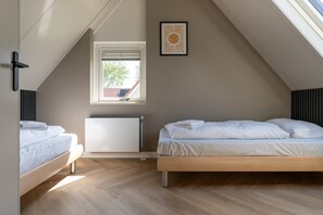 Un dormitorio con dos camas, una ventana, un radiador y un cuadro en la pared.