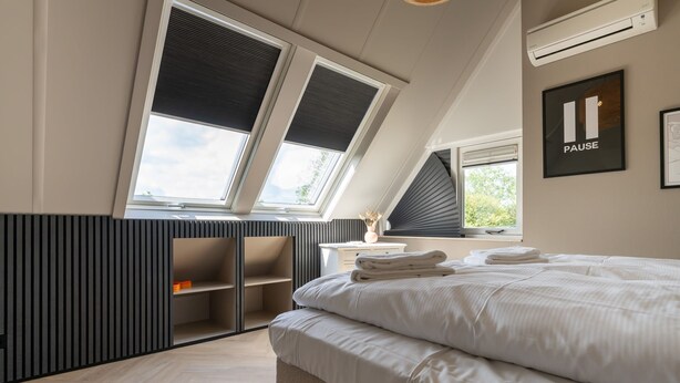 A bedroom with a large bed, skylight windows, a bedside table, and a wall-mounted air conditioner.