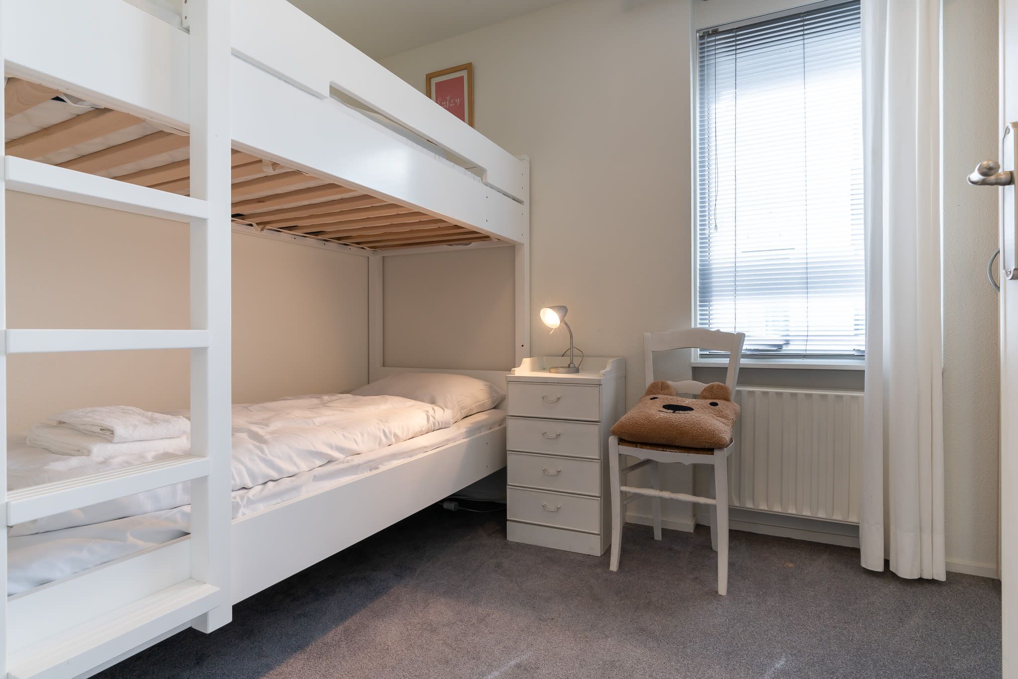Habitación con literas, escritorio, silla y ventana con persianas.