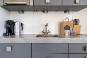 A modern kitchen with a stainless steel sink, a coffee maker, a kettle, and a knife block.