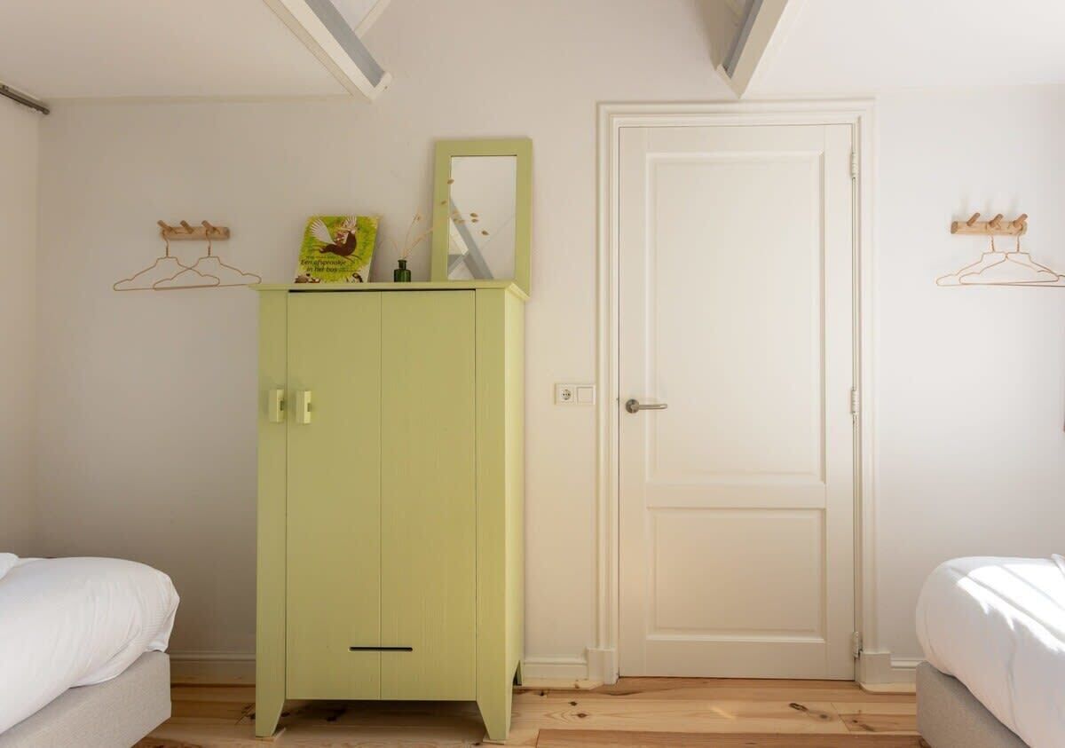 A room with a light green wardrobe, a white door, and two beds.