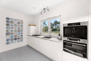 Una cocina moderna con armarios blancos, un horno negro y una ventana con vista a árboles.
