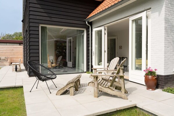 A patio with two wooden chairs and a table, a potted plant, and a sliding glass door leading to an interior space.