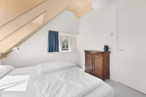 A bedroom with a sloped ceiling, a window with curtains, a wooden cabinet, and a white door.