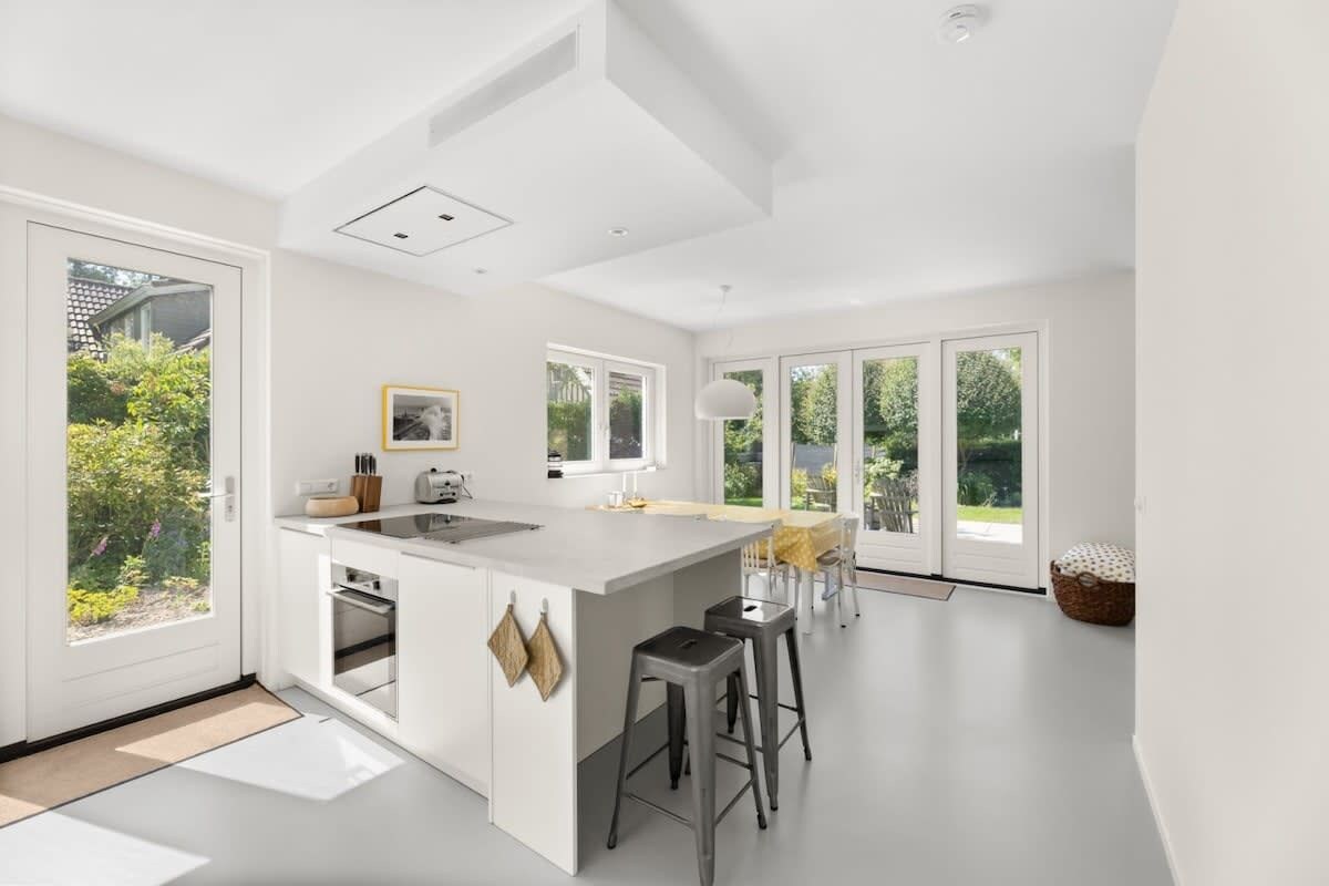 A modern kitchen with a central island, large windows, and a view of greenery.