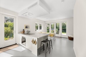 A modern kitchen with a central island, large windows, and a view of greenery.